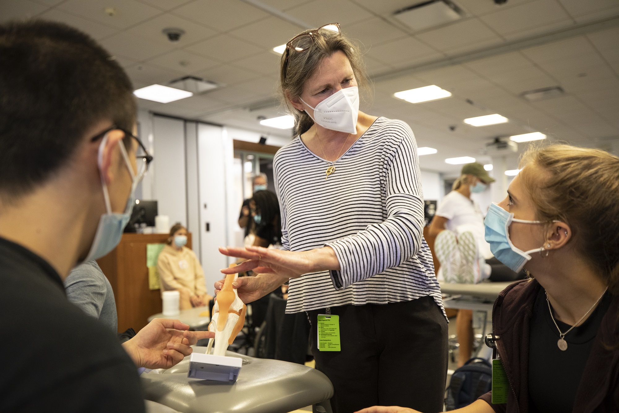 woman points to a model of a knee while two masked students look on