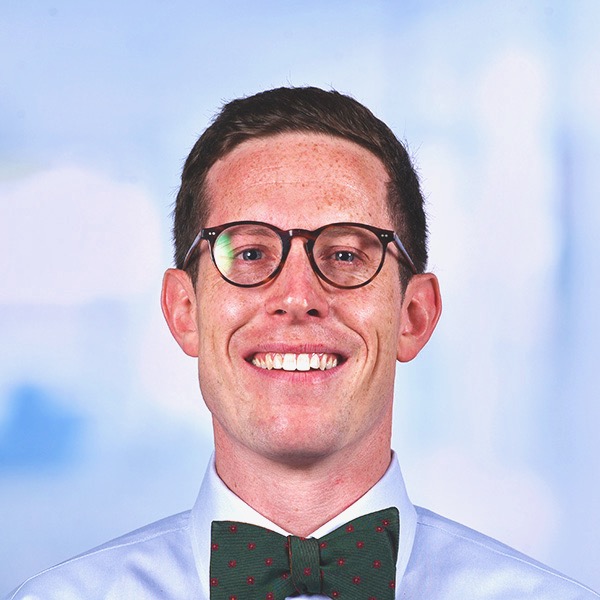 Alex Wolf wearing glasses and in light blue shirt and green bowtie