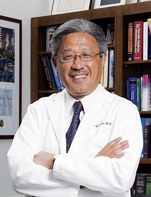 dr dzau stands in front a bookshelf with his arms crossed in a friendly manner