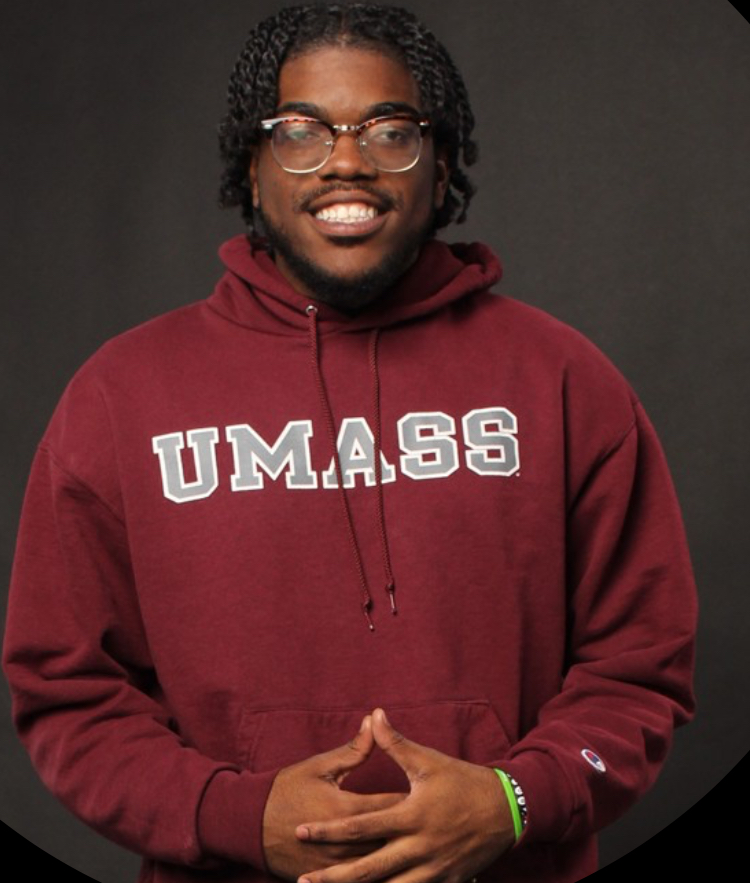 Ronald Dessources has glasses and black braids. He is wearing a red UMASS sweatshirt.