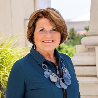 pam has short reddish brown hair and wears a blue jacket