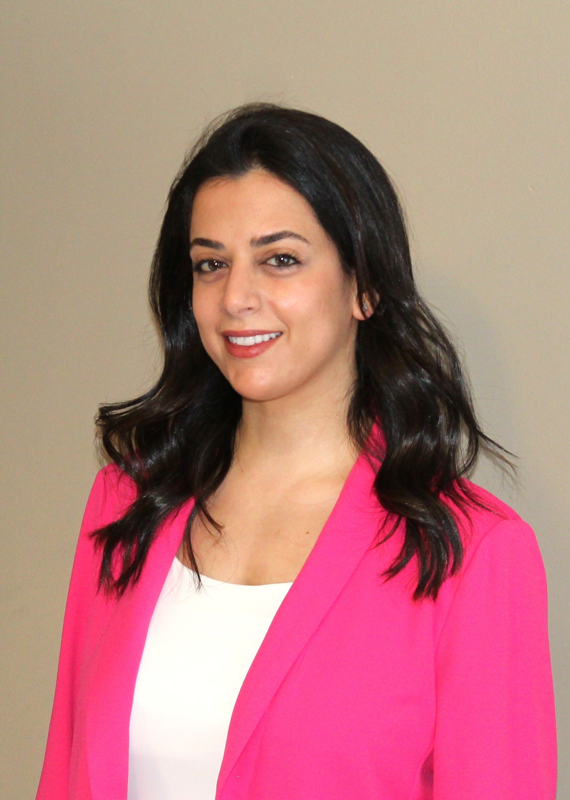 Ingrid Korbani has long black hair and is wearing a white shirt and hot pink blazer