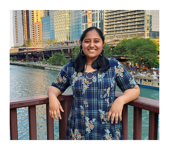 Akshaya stands on a deck in front of a river with golden afternoon light