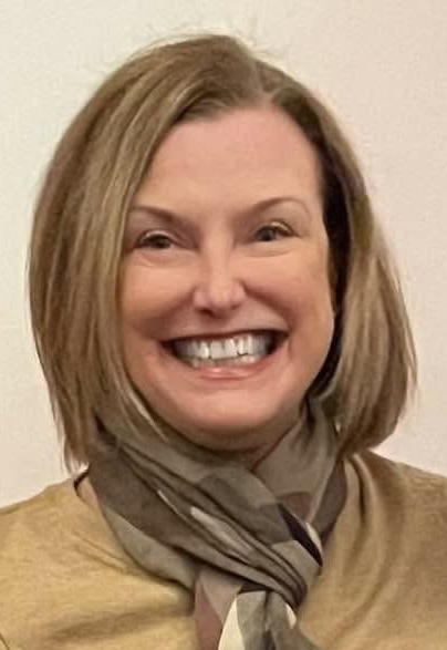 Woman with blonde hair smiling and wearing a green shirt and scarf