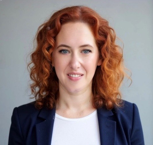 Headshot of Woman with wavy red hair wearing a white shirt and a blue jacket