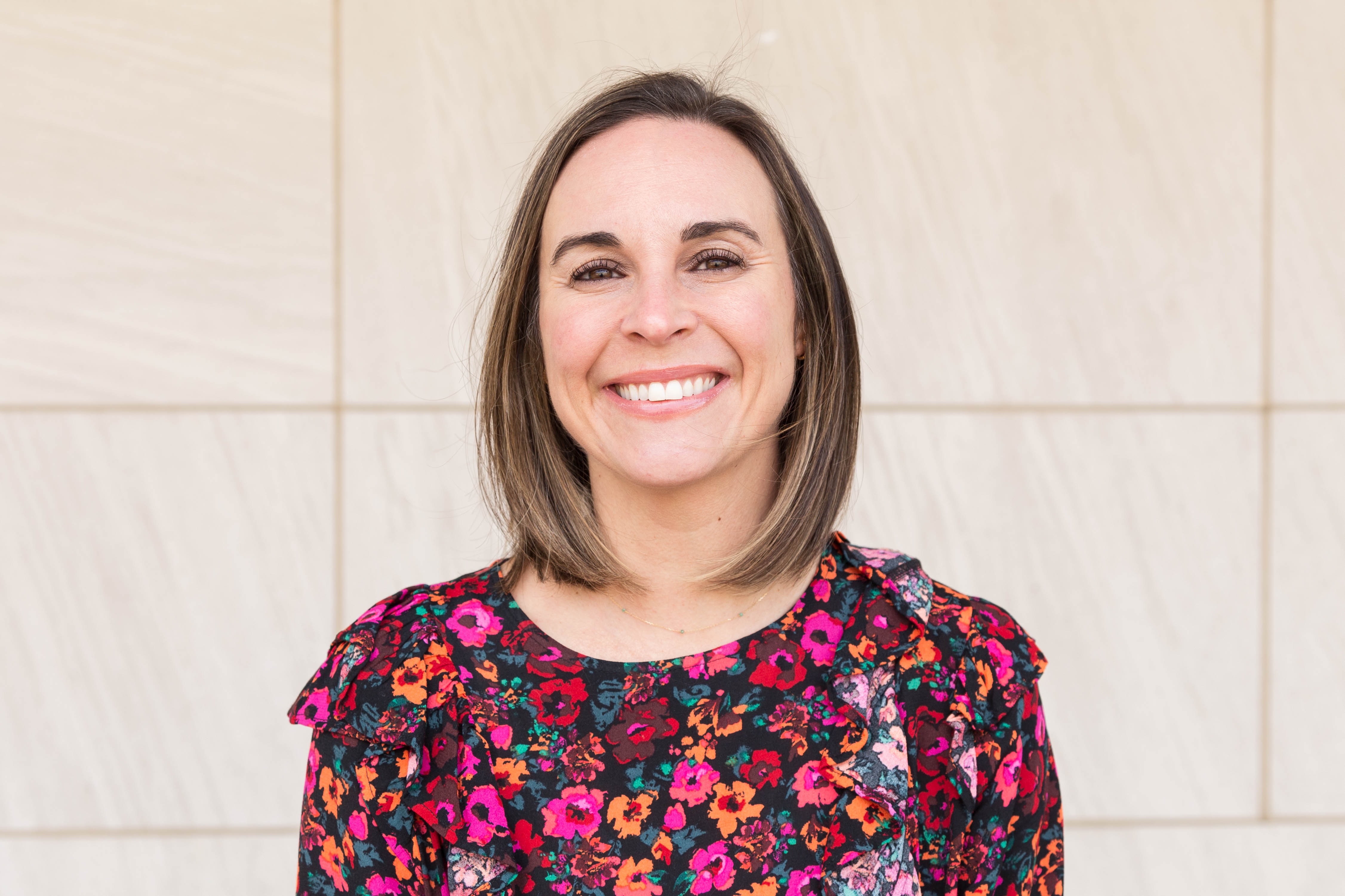 Headshot of woman with shoulder length brown hair smiling at camera and wearing floral shirt