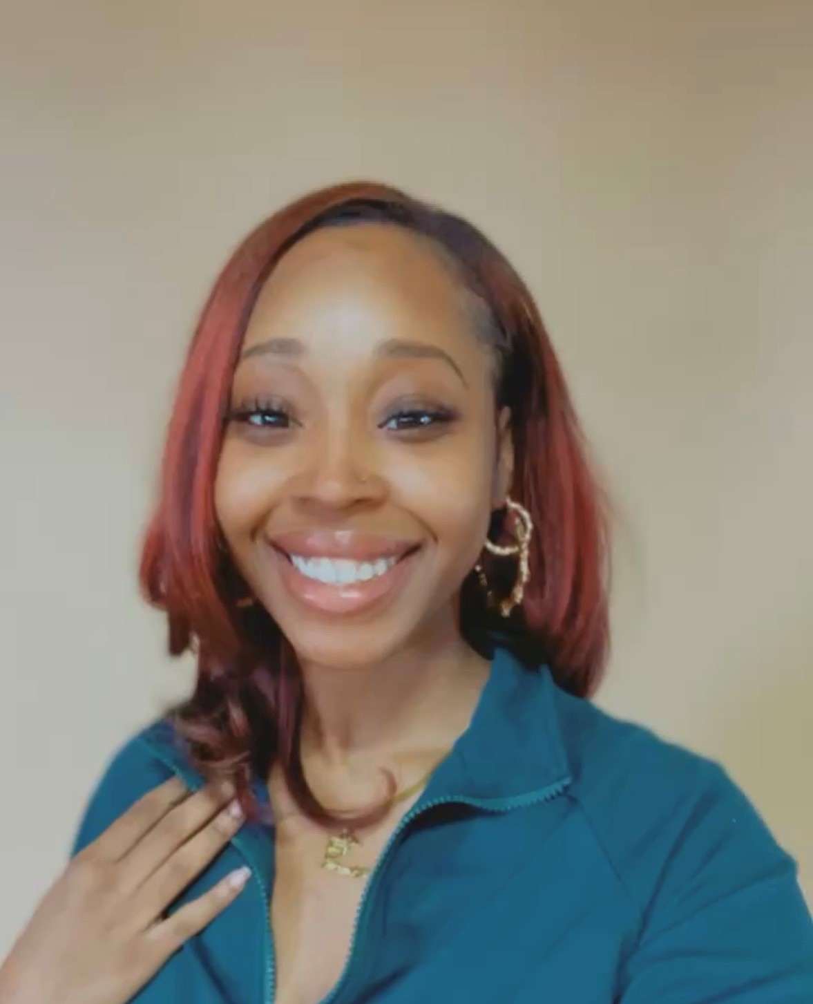 Headshot of a woman with dyed red hair smiling at the camera and wearing a blue shirt
