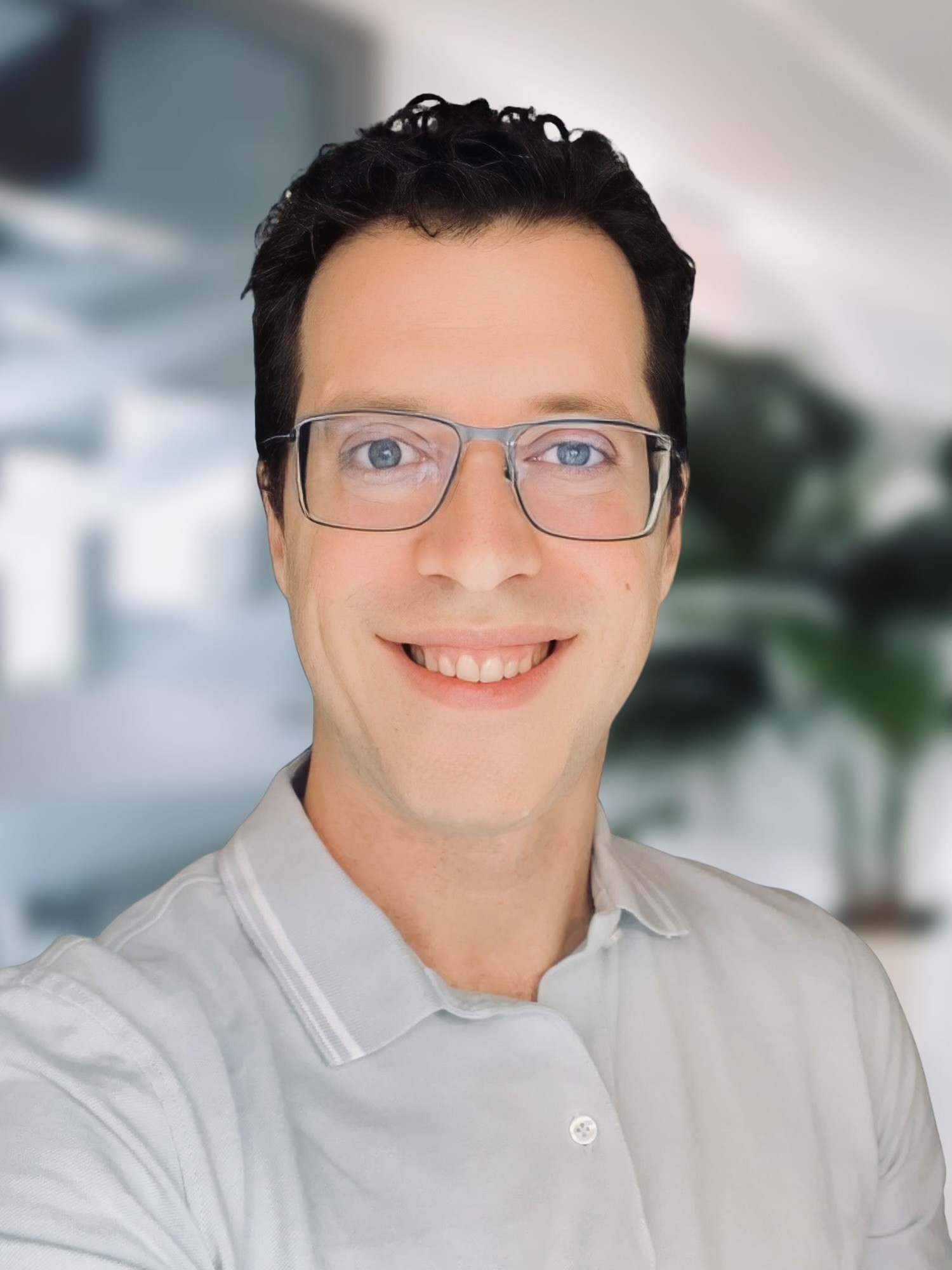 Headshot of man with short black hair wearing glasses and a gray polo shirt in front of a blurred background