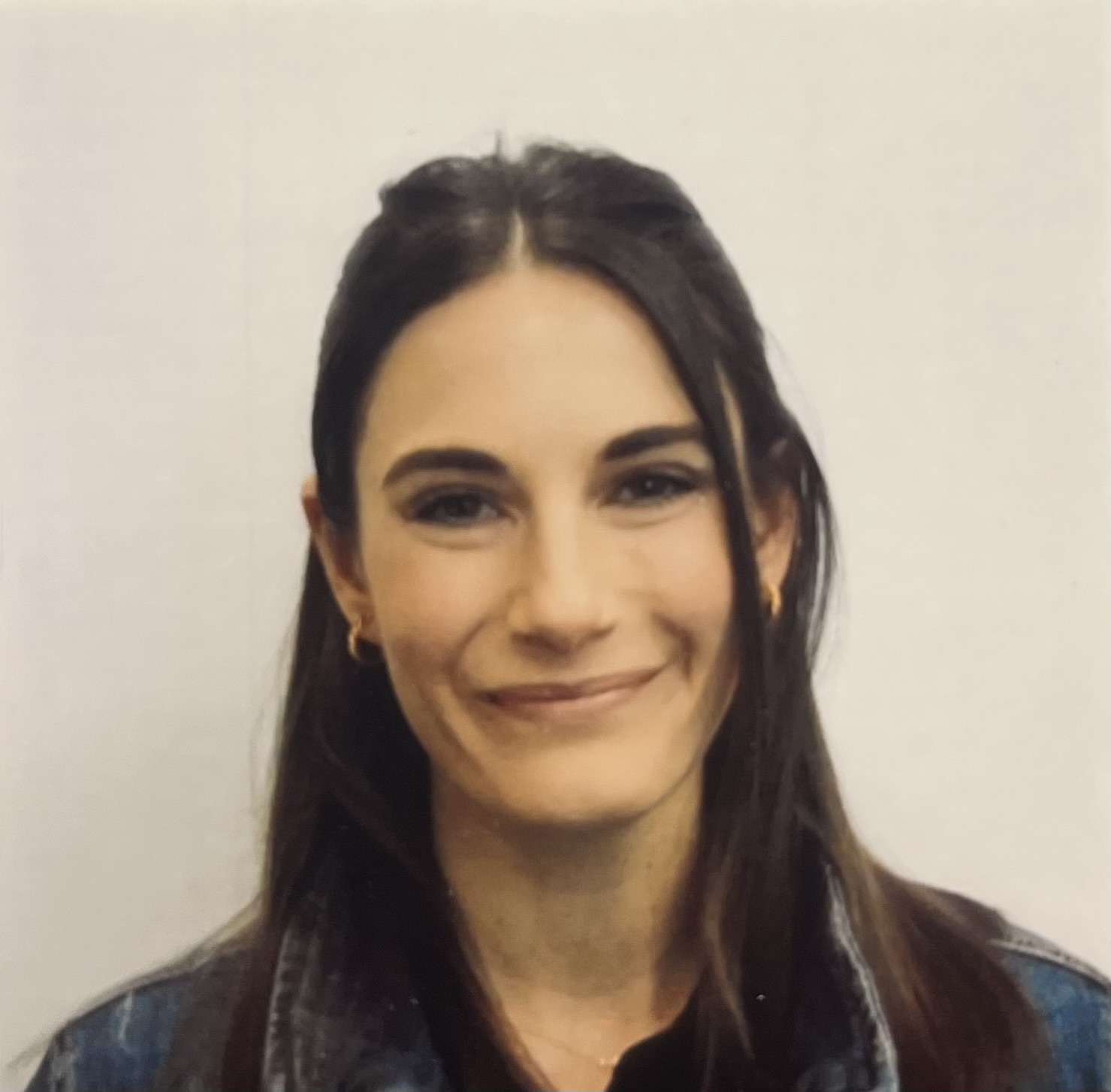 Headshot of woman with long dark hair wearing a dark blue jacket in front of a solid white background.