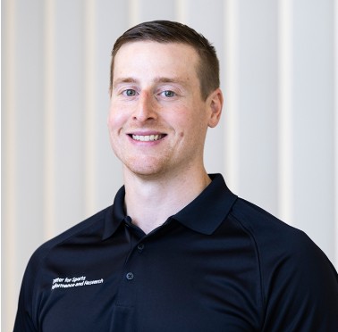 Photo of man with short hair wearing a black collared shirt in front of a white background