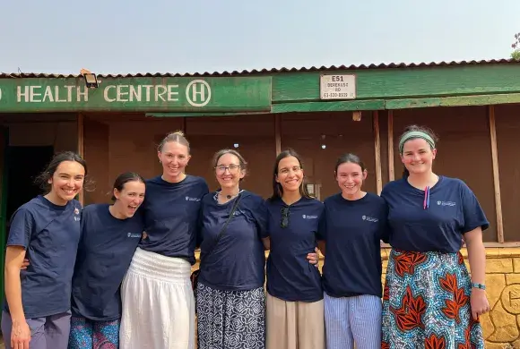 Seven women stand next to each other posing for a photo in front of a health center