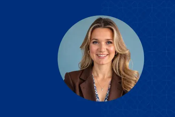 Woman with blonde hair smiling and wearing a brown jacket