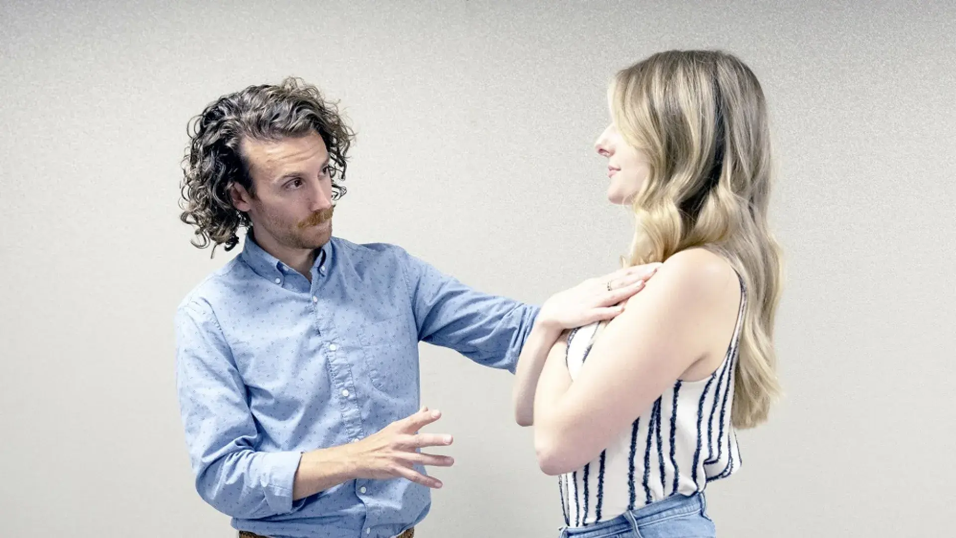 man helps woman who has her arms crossed to stand straight