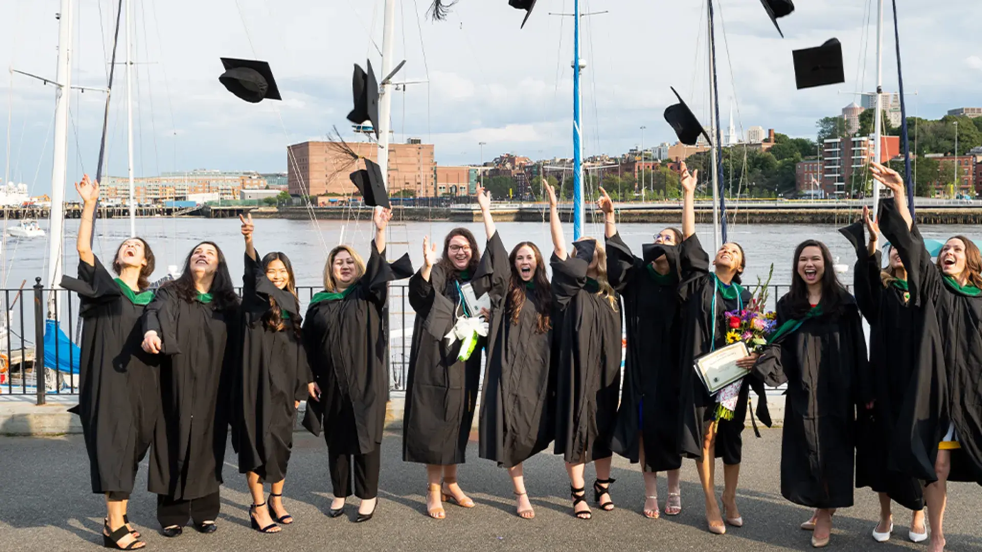 women wear black graduation robes and toss their graduation caps in the air