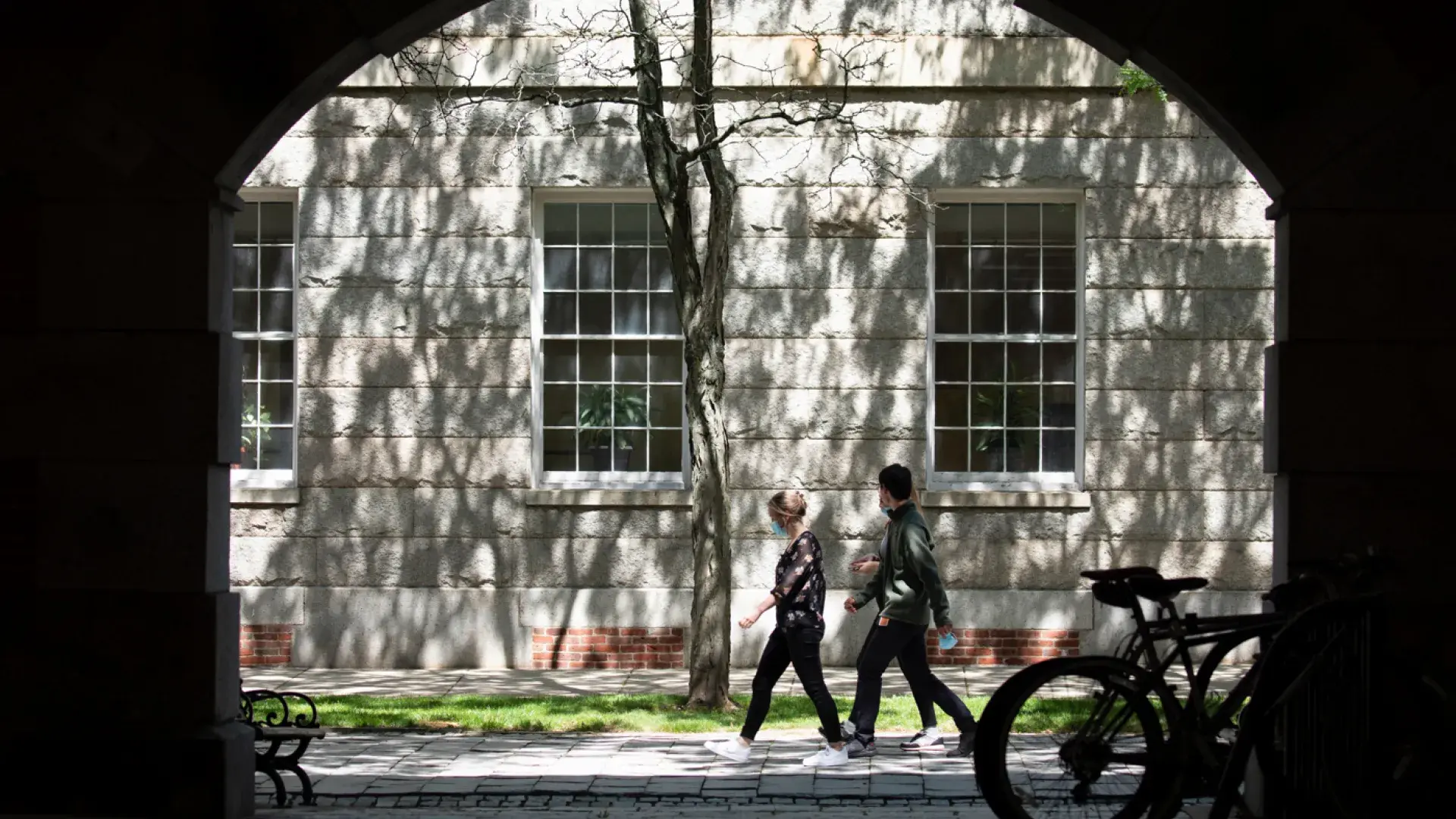 Two people walking on a sidewalk next to a building