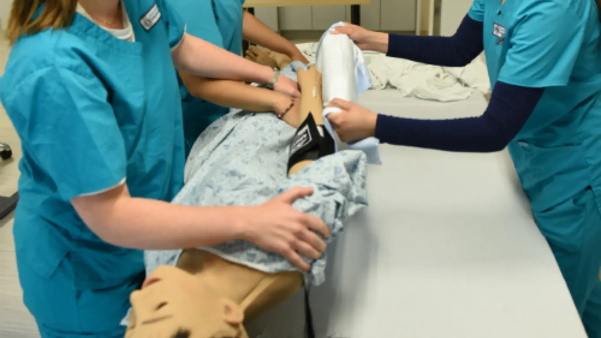 BSN students (l-r) Victoria Ryan, Stacy Conceicao, and Natalie Mata working with a manikin of color in the Shouse Building Nursing Lab.