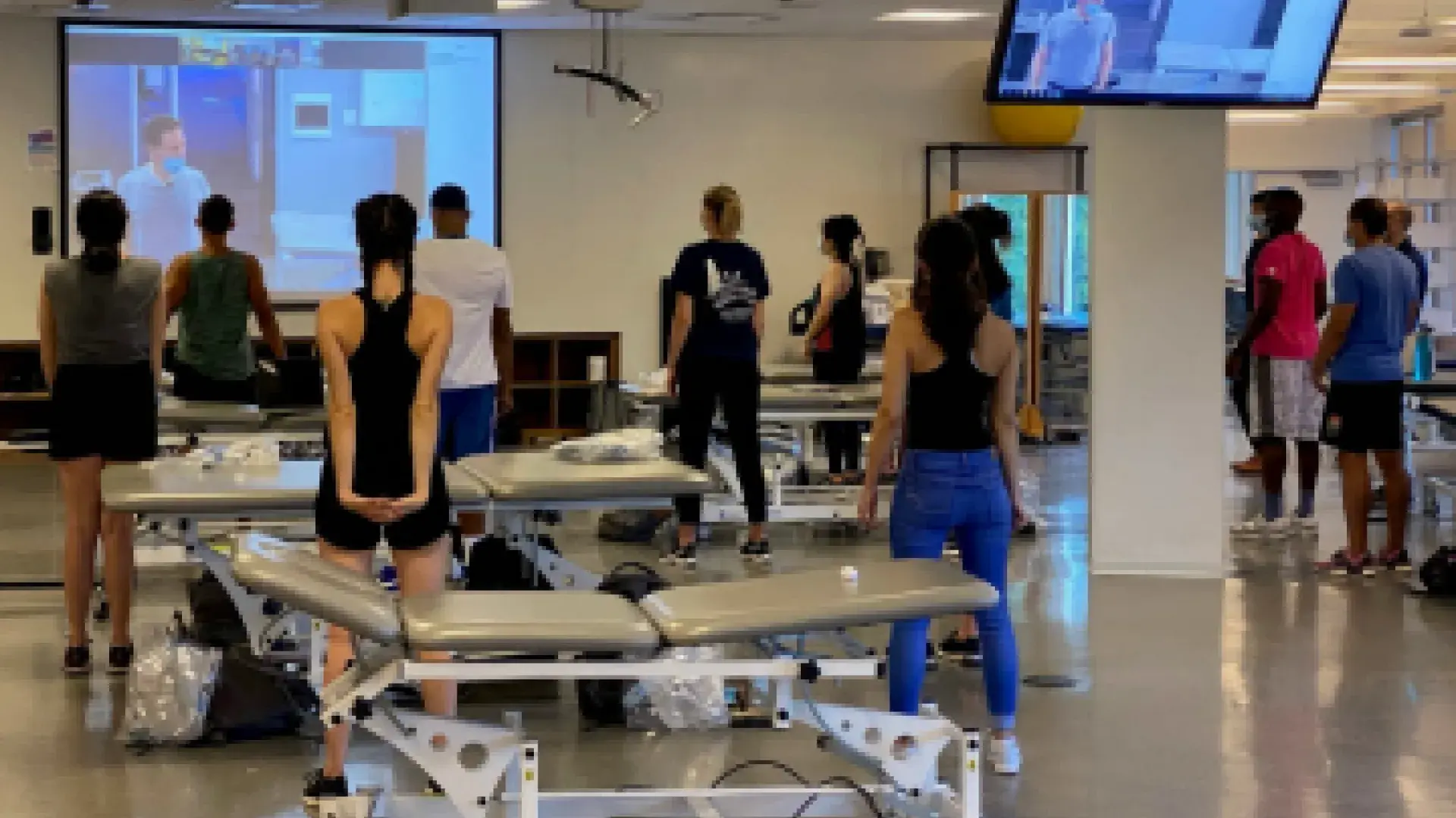 DPT students, adhering to social distancing standards, watch Associate Professor Doug Gross as he works with the other half of the class in an adjacent room.