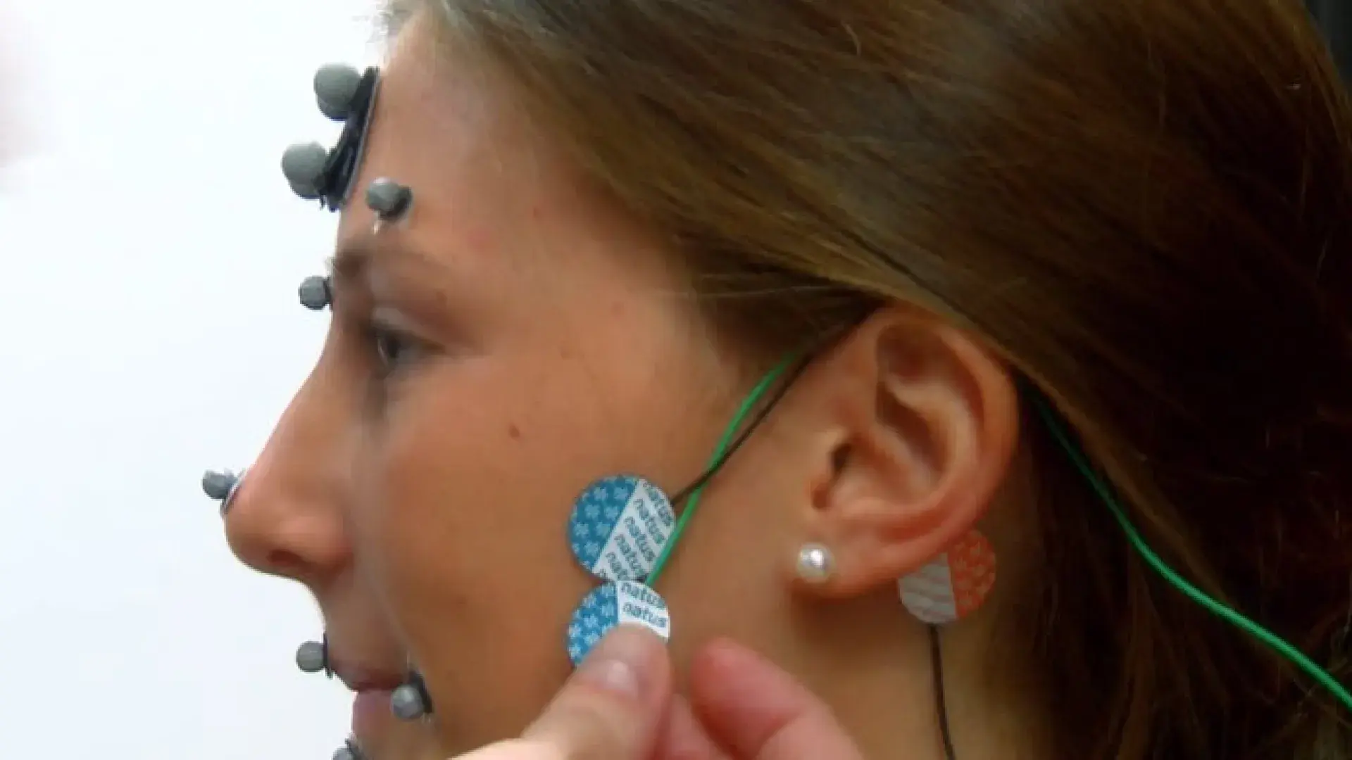 A brown-haired woman's head in profile has sensors placed under her temple and below her ear