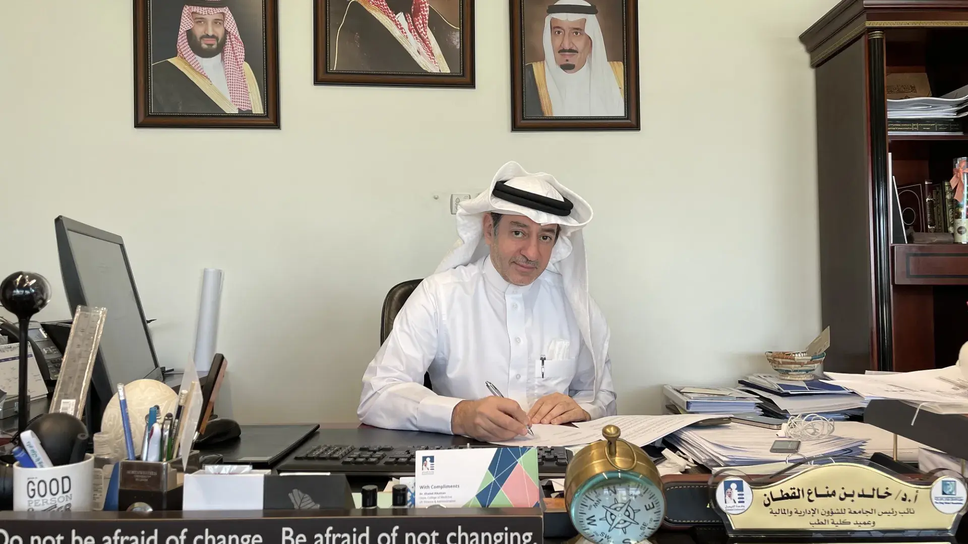 man in white shirt and Kaffiyeh sits at a large desk with a pen to paper