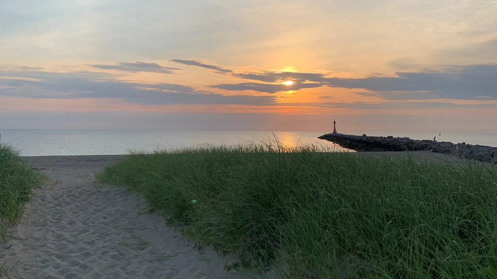a path through a sand dune leads to the beach and sunrise