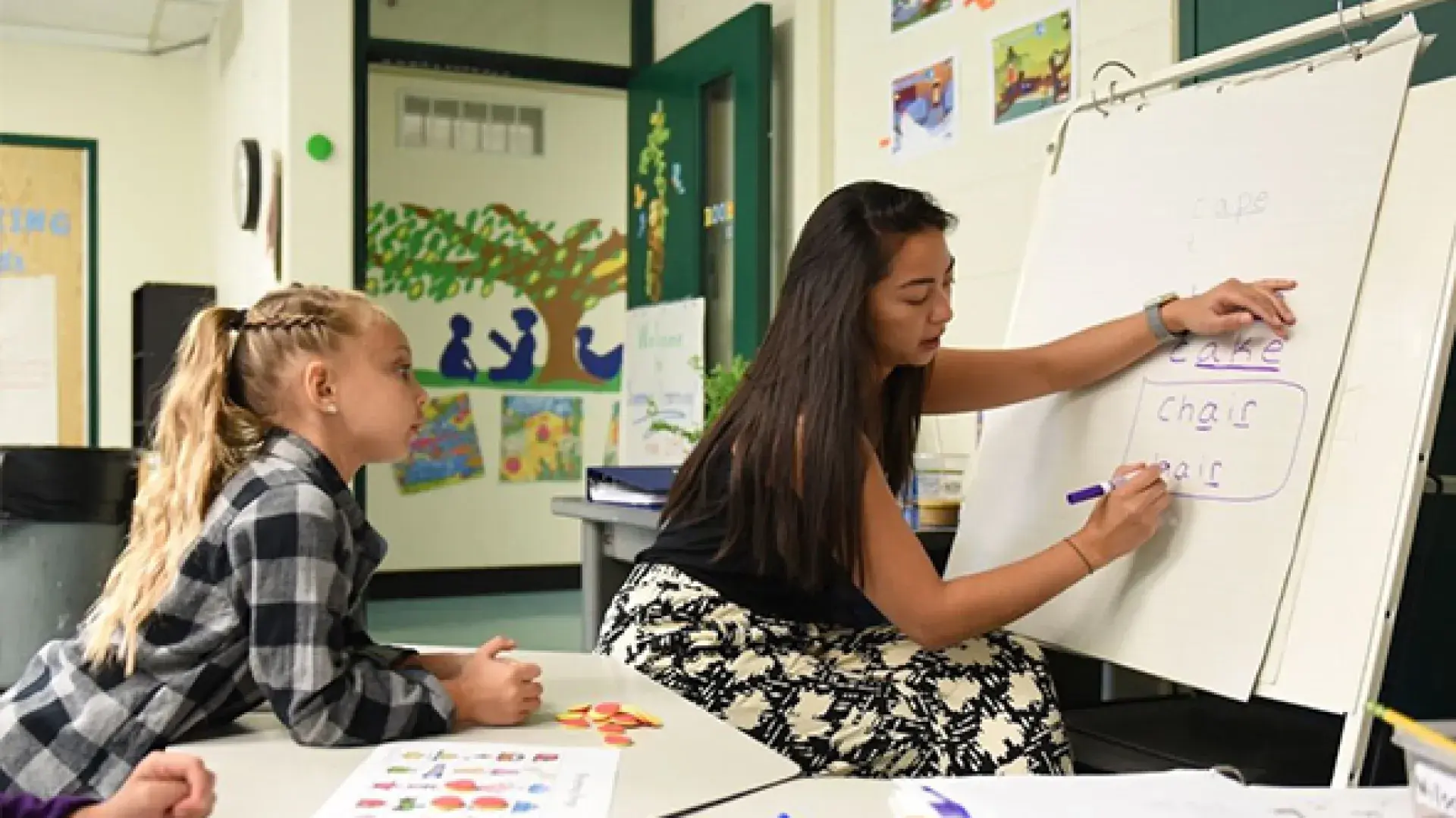 young woman writes letters on a paper easel in an elementary classroom