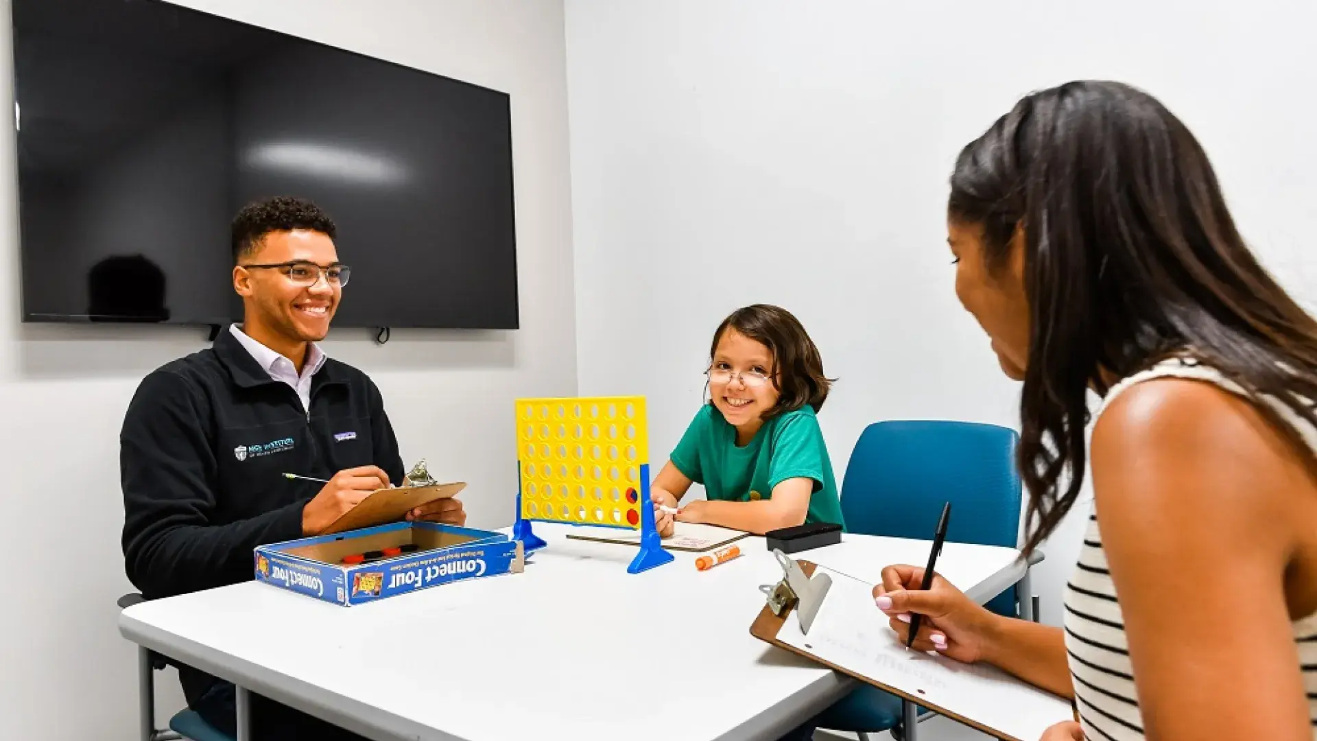 a child plays connect four with two student clinicians