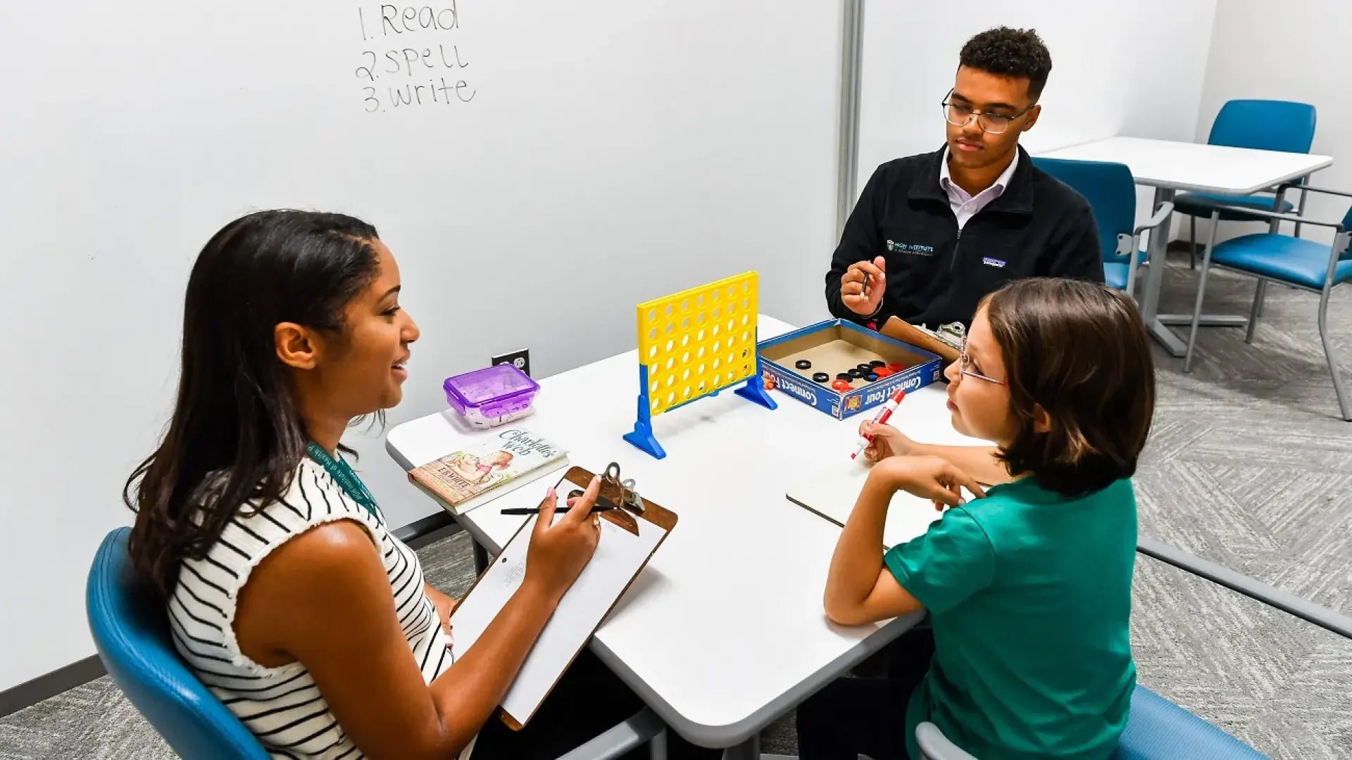 A group therapy session with two adults working with a young child on speech and language intervention techniques using games. This image is relevant to clinical practicum for SLPs and graduate speech pathology programs.