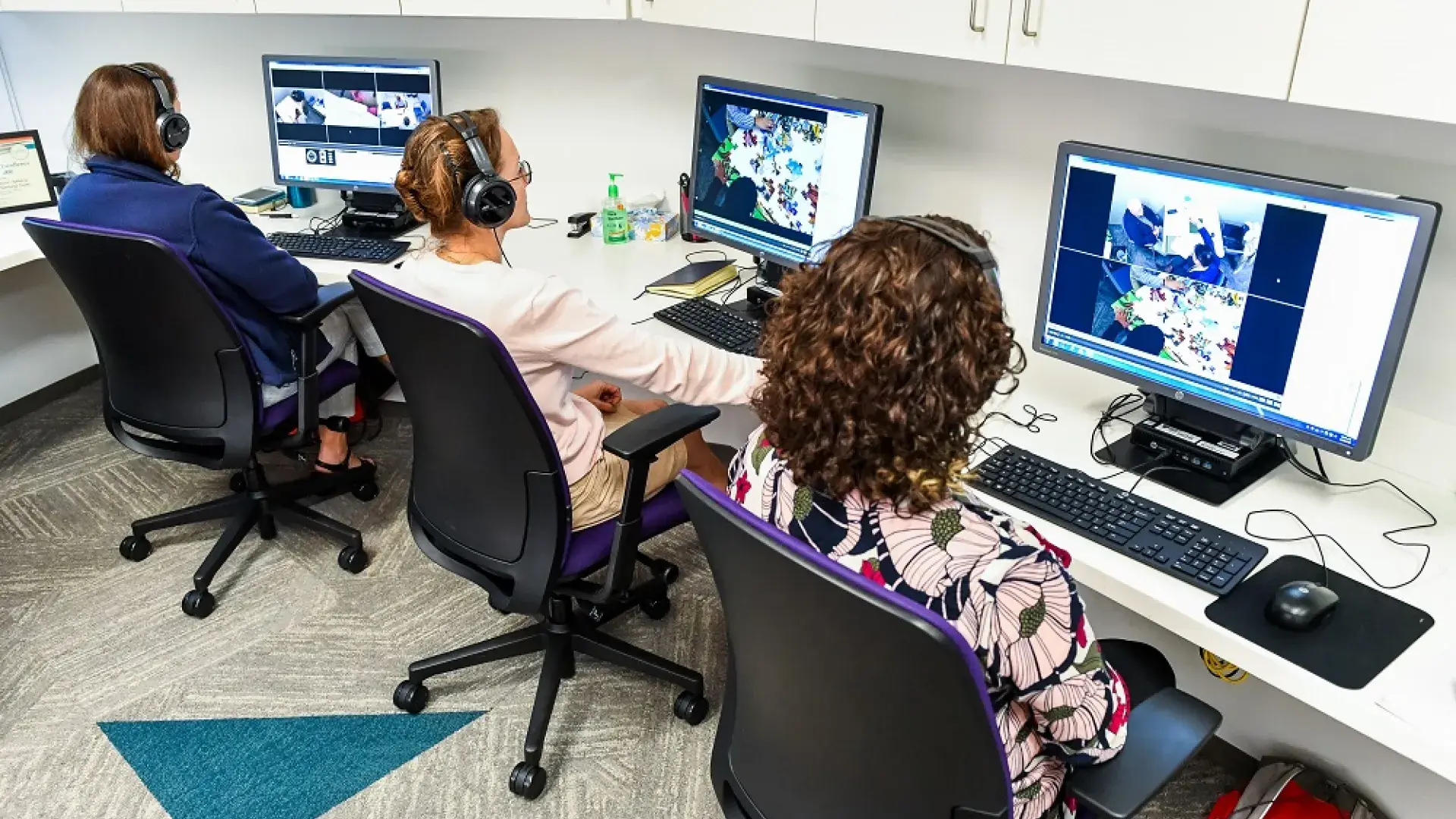 three women sit at computers with headphones on