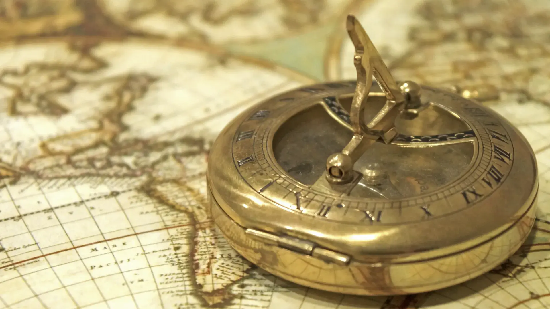 a golden compass sits on an antique sepia toned map