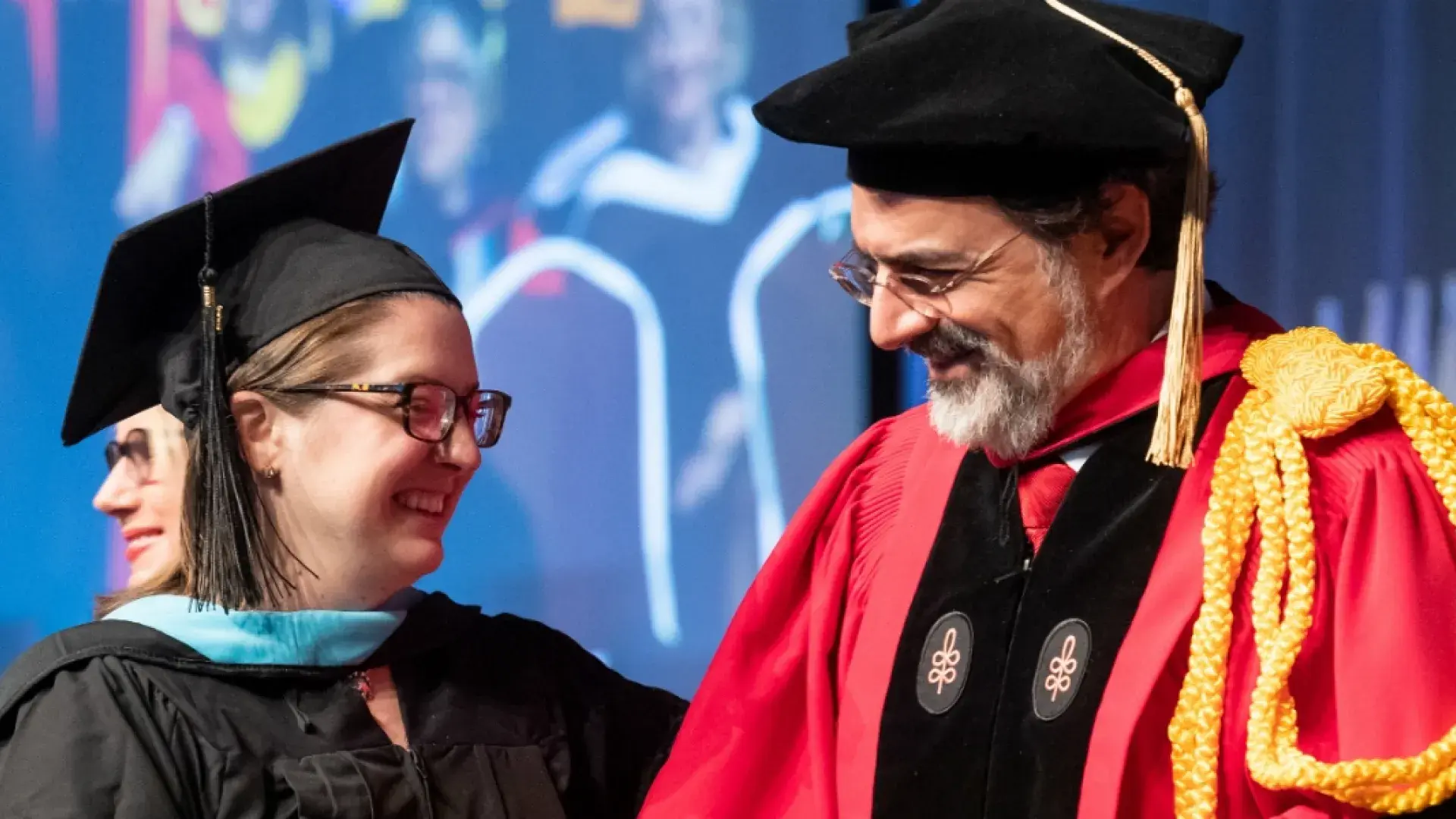 a man in graduation cap and gown smiles at a woman in graduation robes