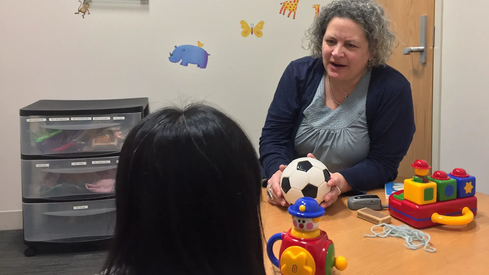 woman holds soccer ball and speaks to a child while seated at a table