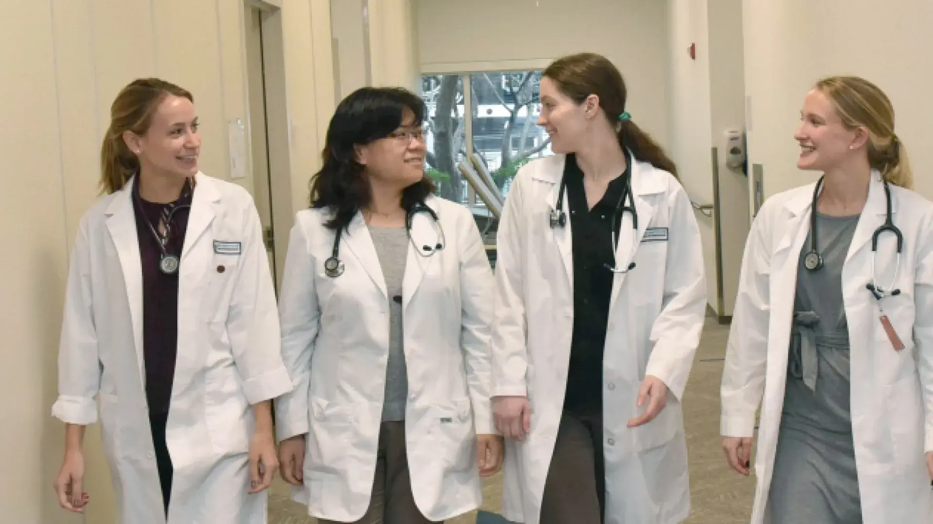 women in white coats walk down hallway
