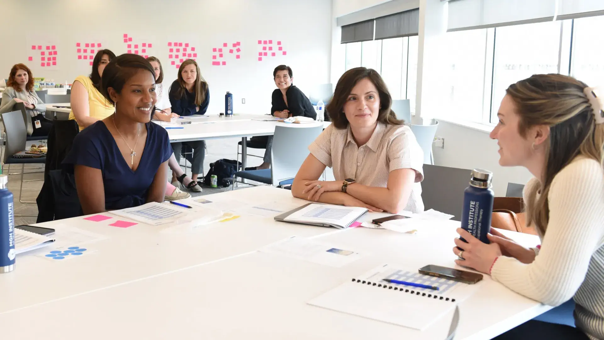women sit around a conference room table with pink postit notes on the wall