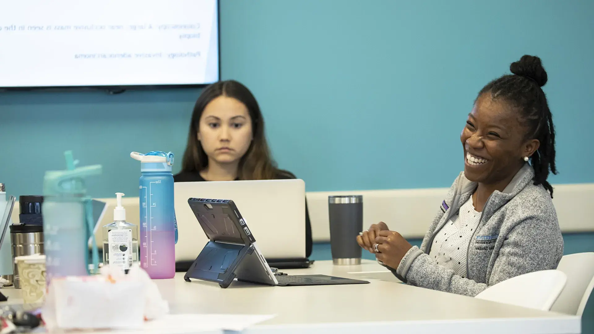 woman laughs at something off camera while she uses her tablet at a table