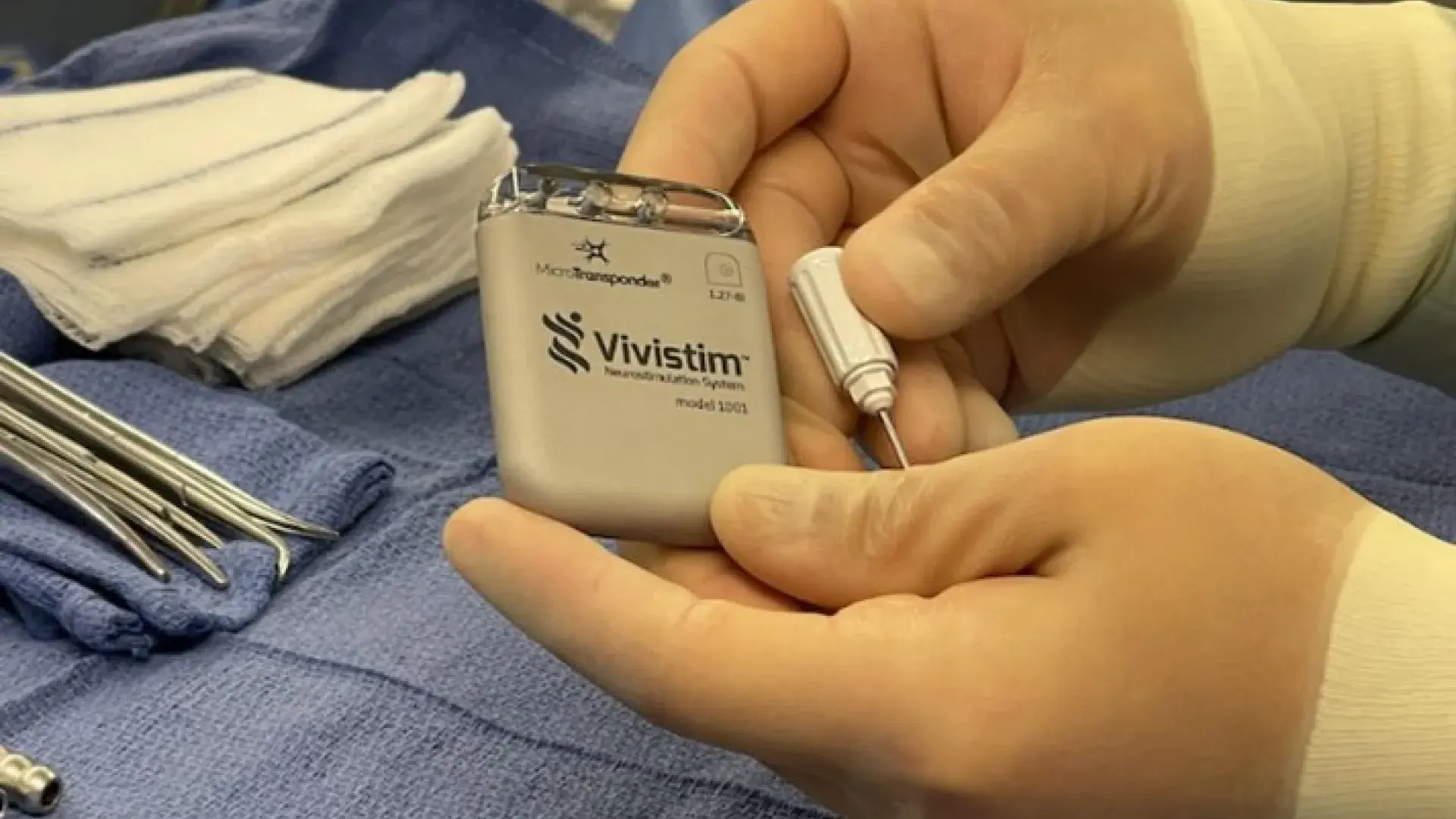 gloved hands hold a grey rectangular device over sterile surgical towel