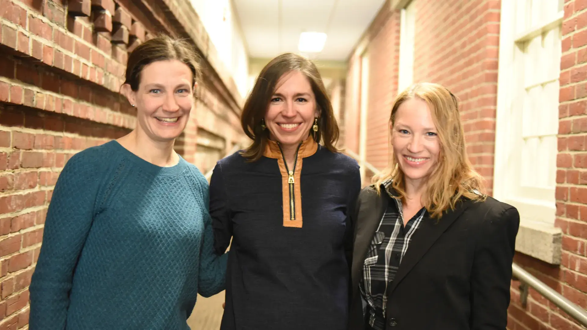 three women stand in a brick hallway