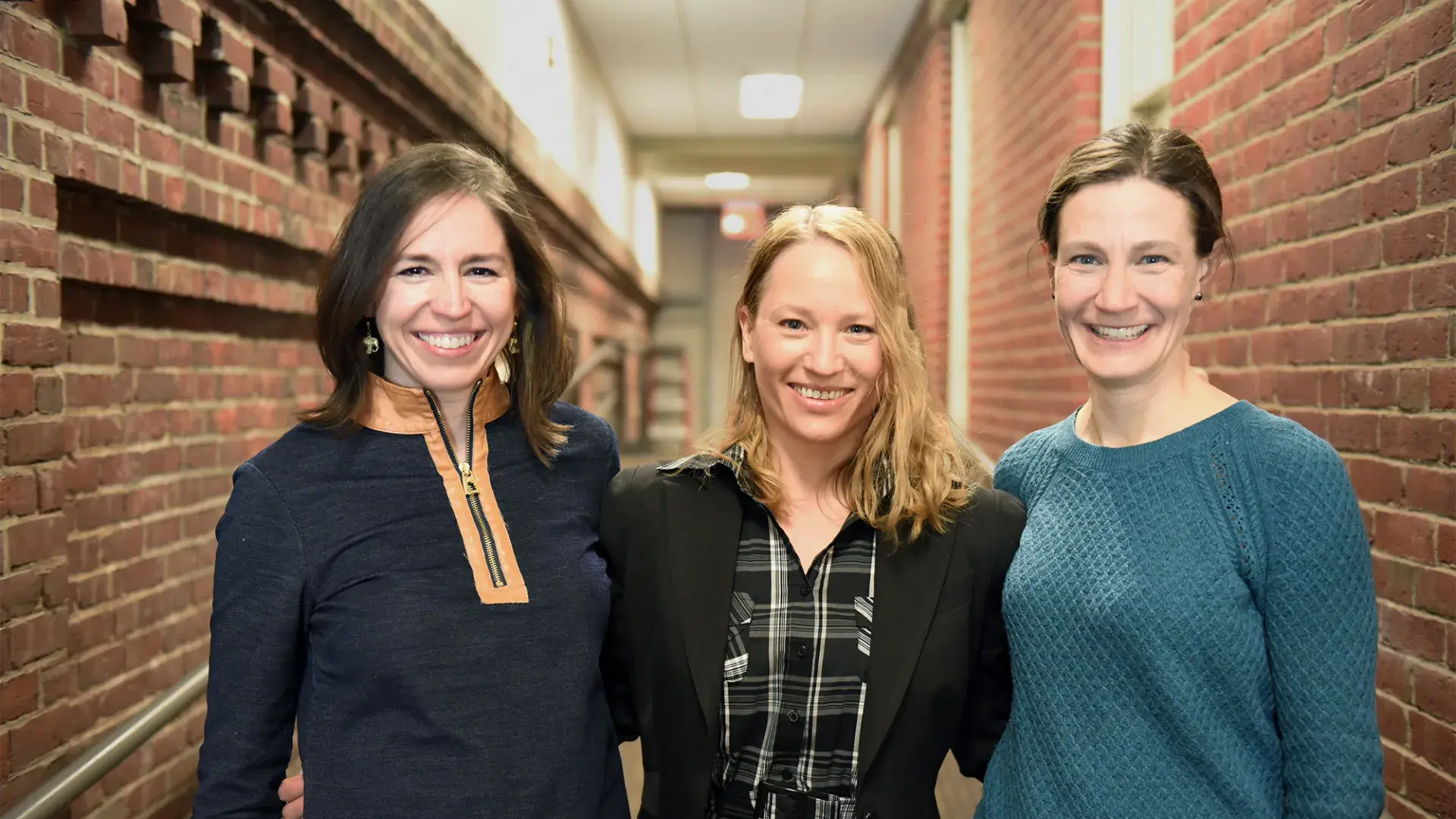 Cognitive Neuroscience Group co-chairs Sofia Vallila Rohter, Yael Arbel, and Lauryn Zipse stand in a brick hallway arm and arm