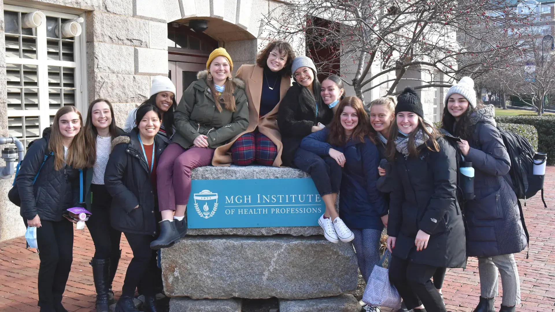 female students sit on a rock that says mgh institute of health professions