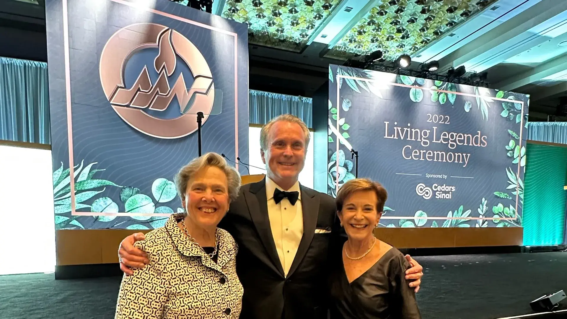 man stands in middle with arms around two women dressed in formal attire