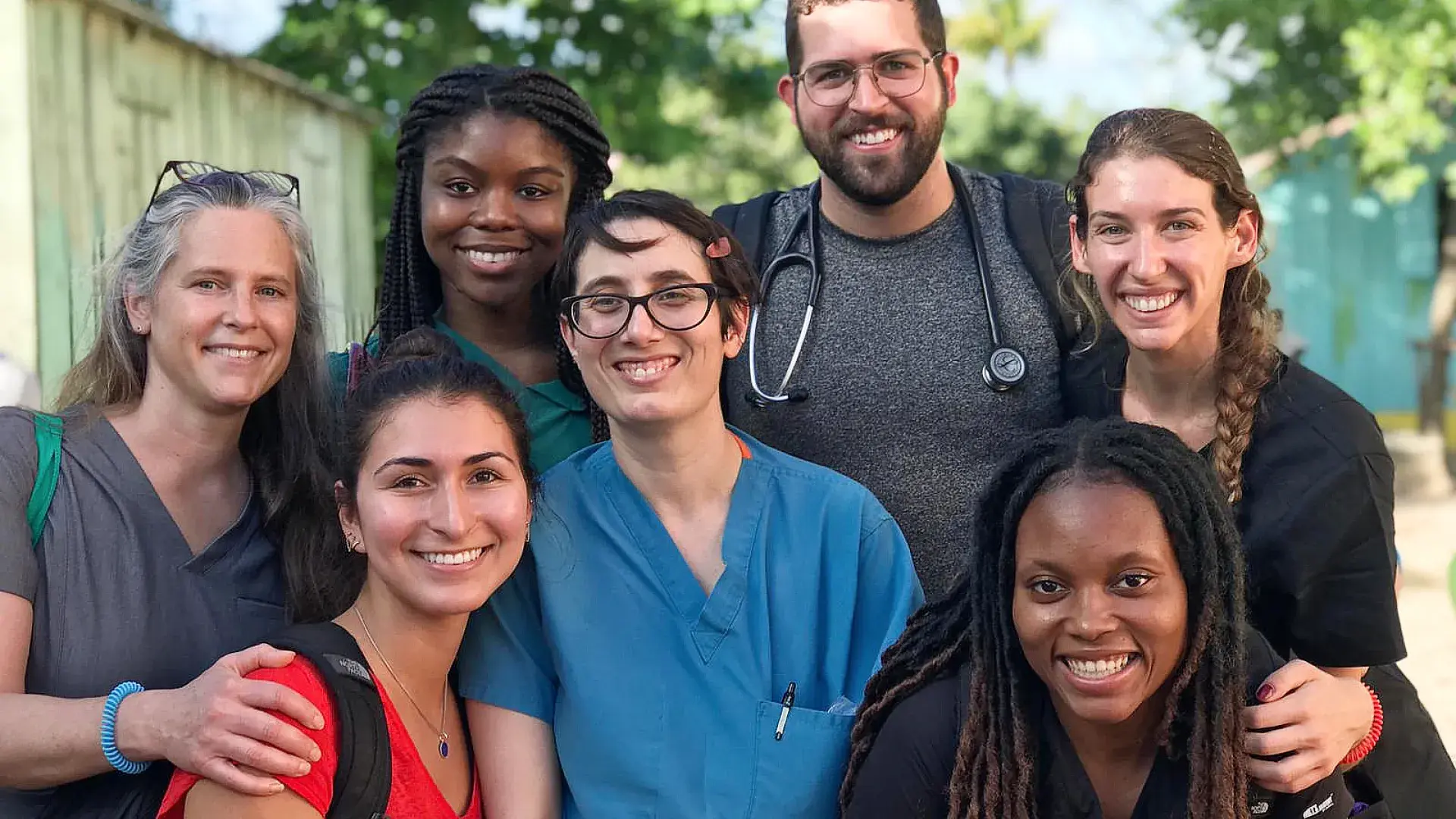 a group of smiling people stand in the street, one wears a stethoscope 
