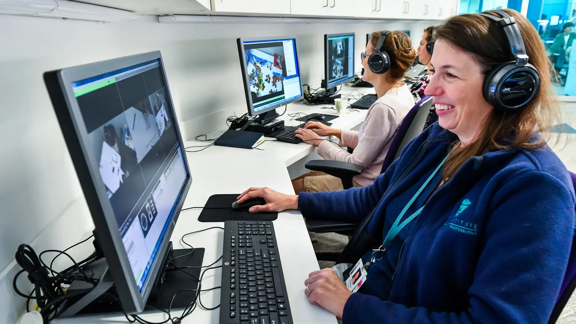 a woman sits with headphones and watches a monitor as another does the same thing next to her