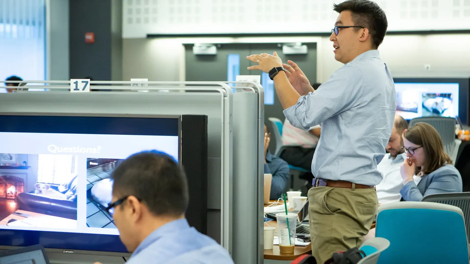 man gestures above students and large screens