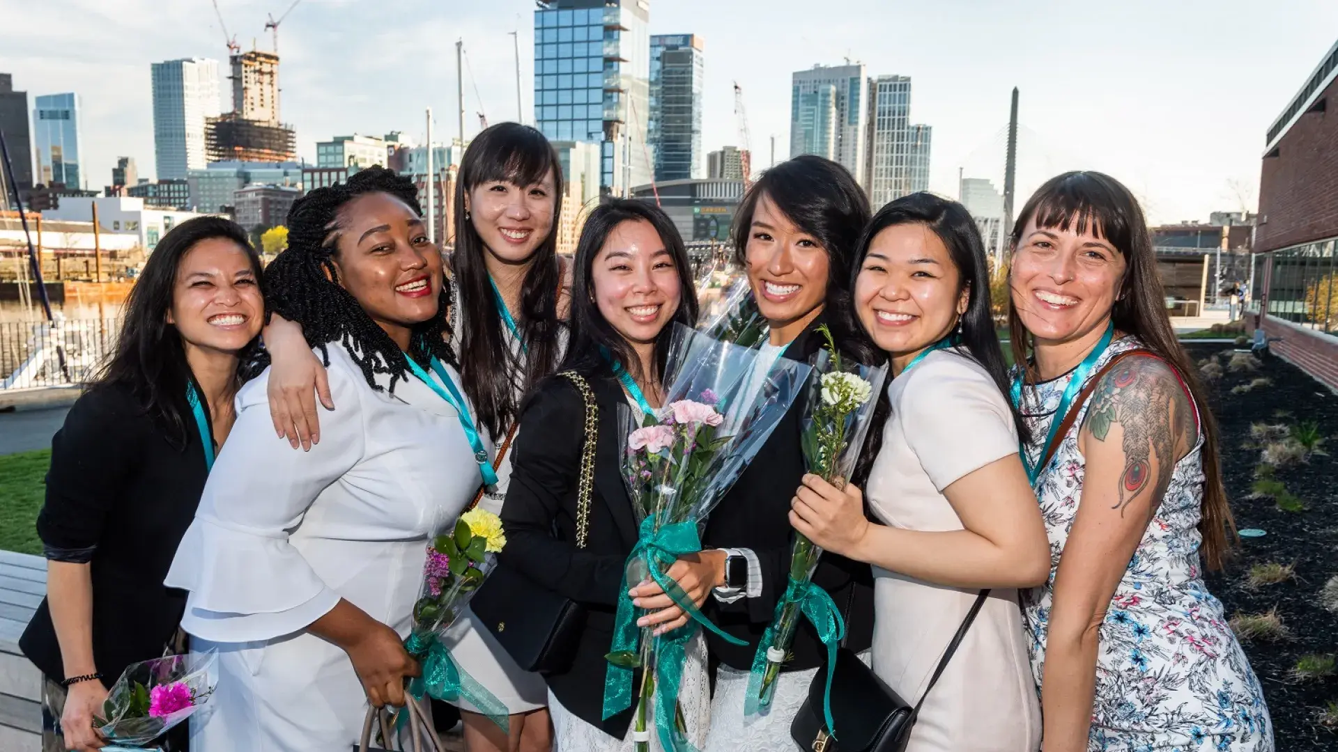 group of women smiles exuberantly some hold flower bouquets 
