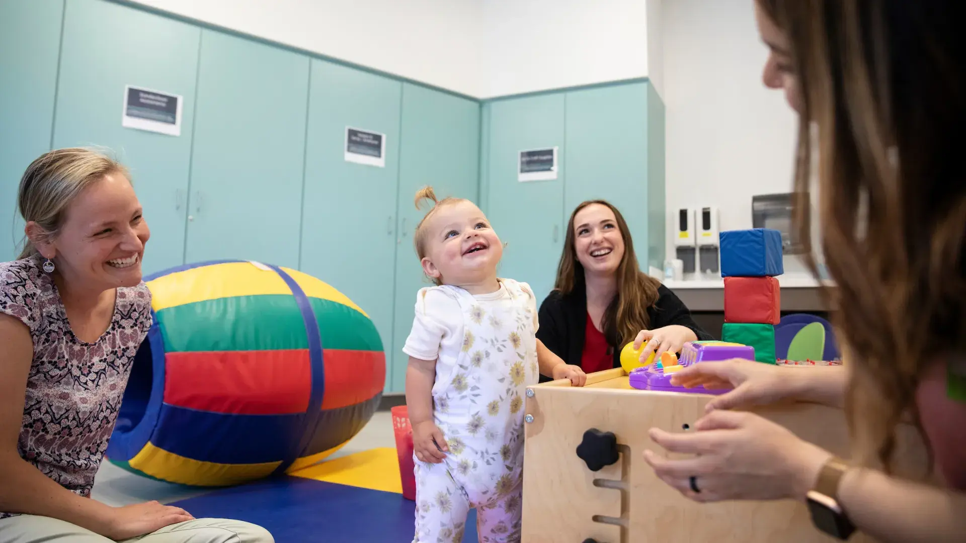 a toddler smiles up at a woman while holding a colorful block
