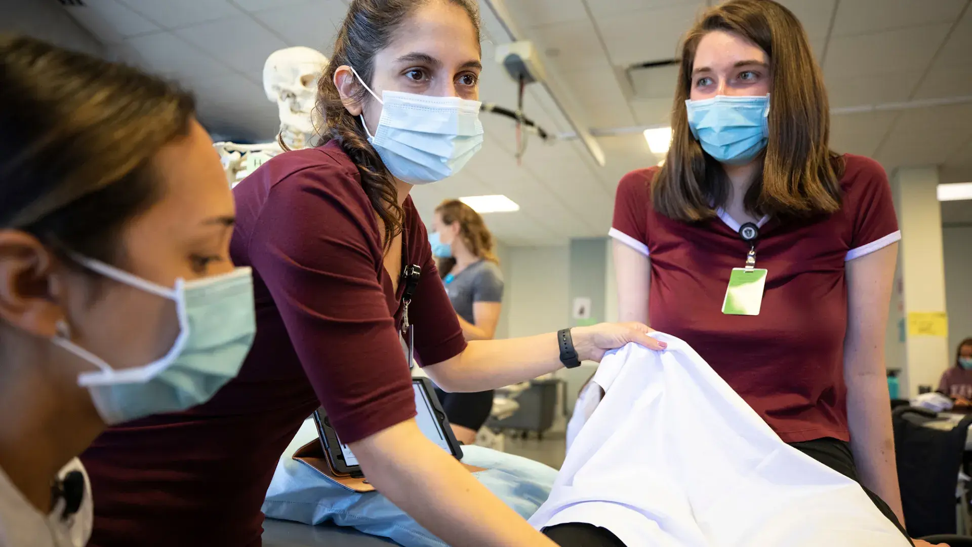 woman holds up cloth in front of another woman on an exam table