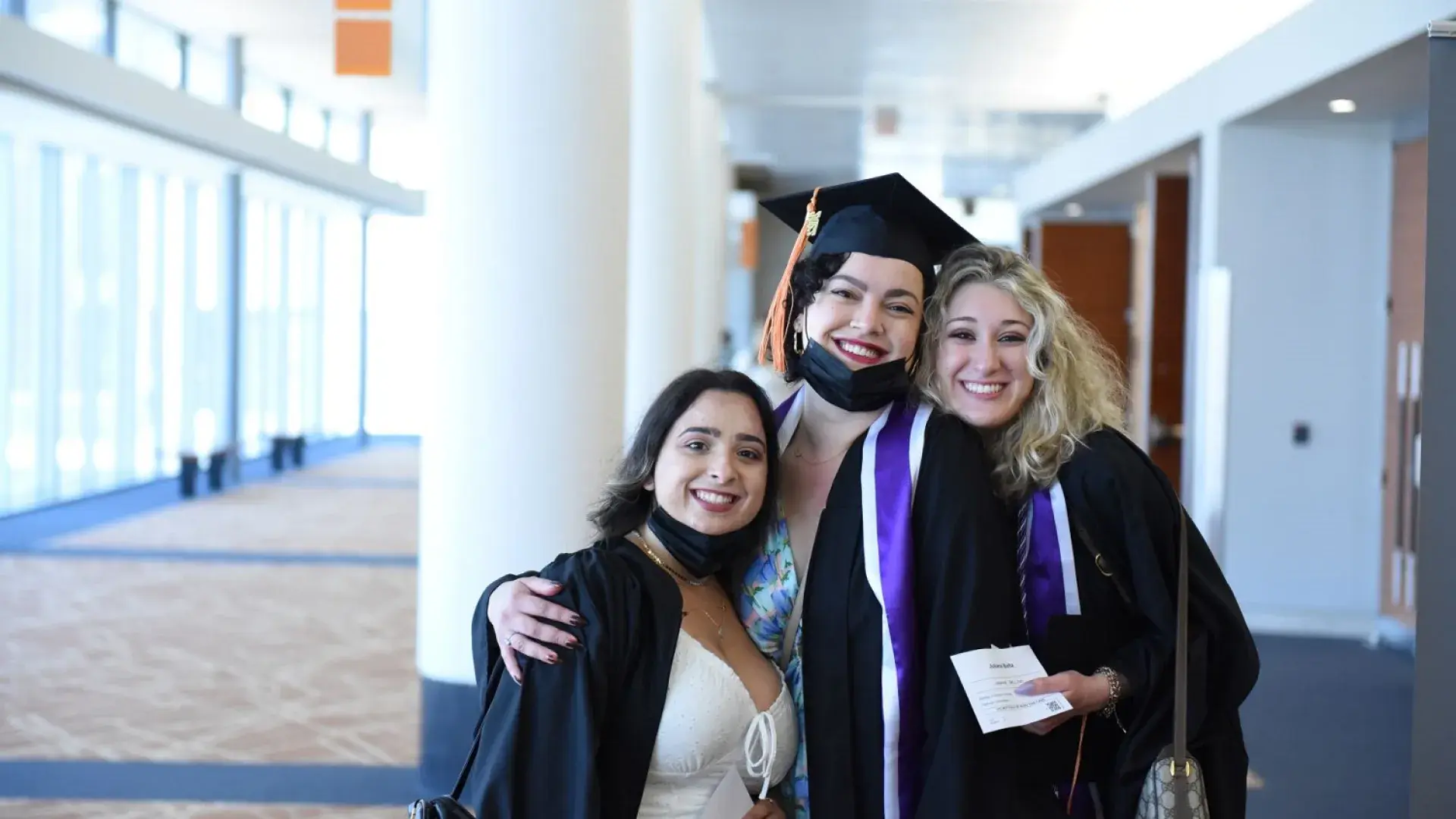 three women stand with their arms around each other in graduation caps and gowns