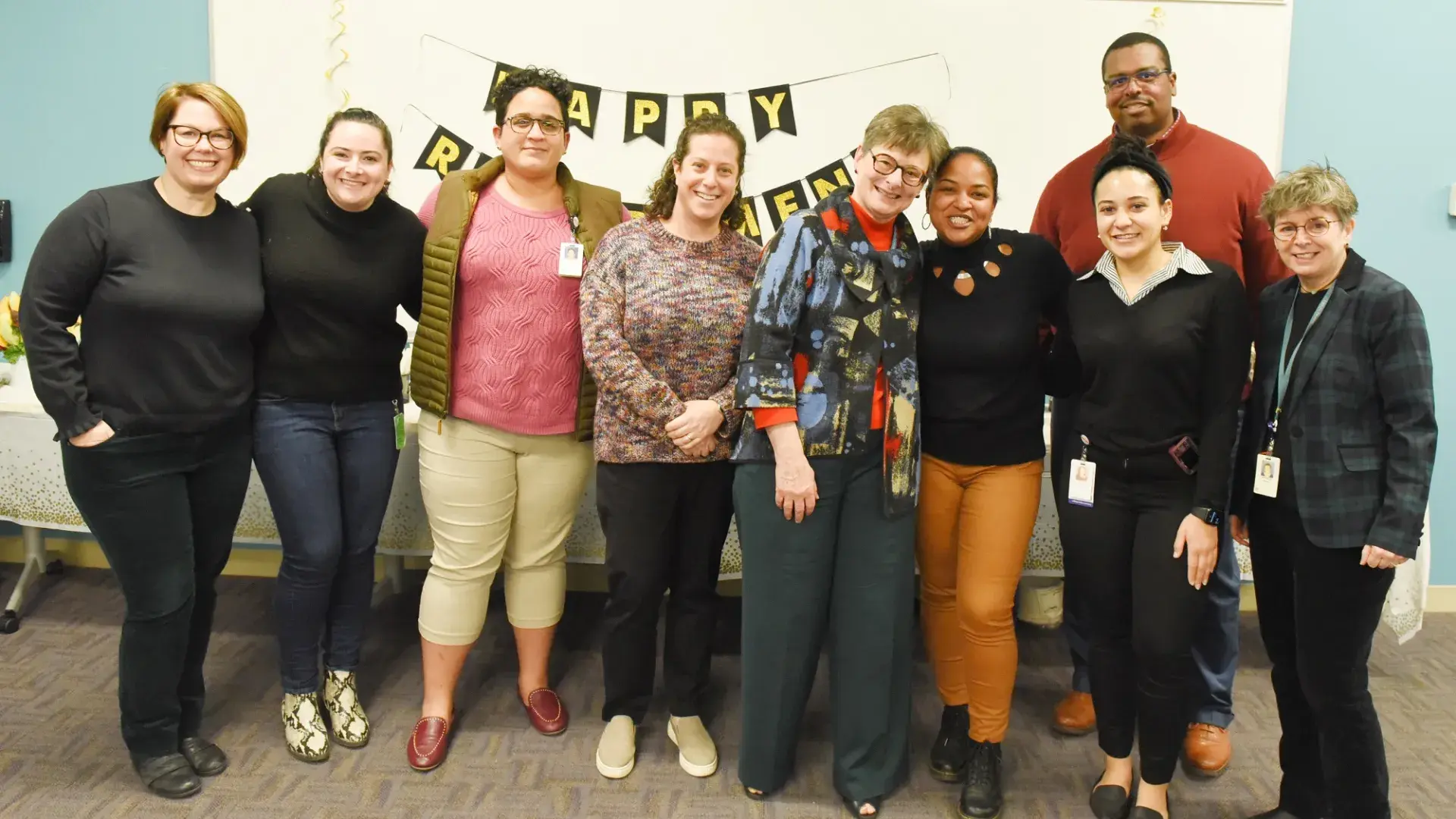 a group of smiling people pose in front of a "happy retirement" banner
