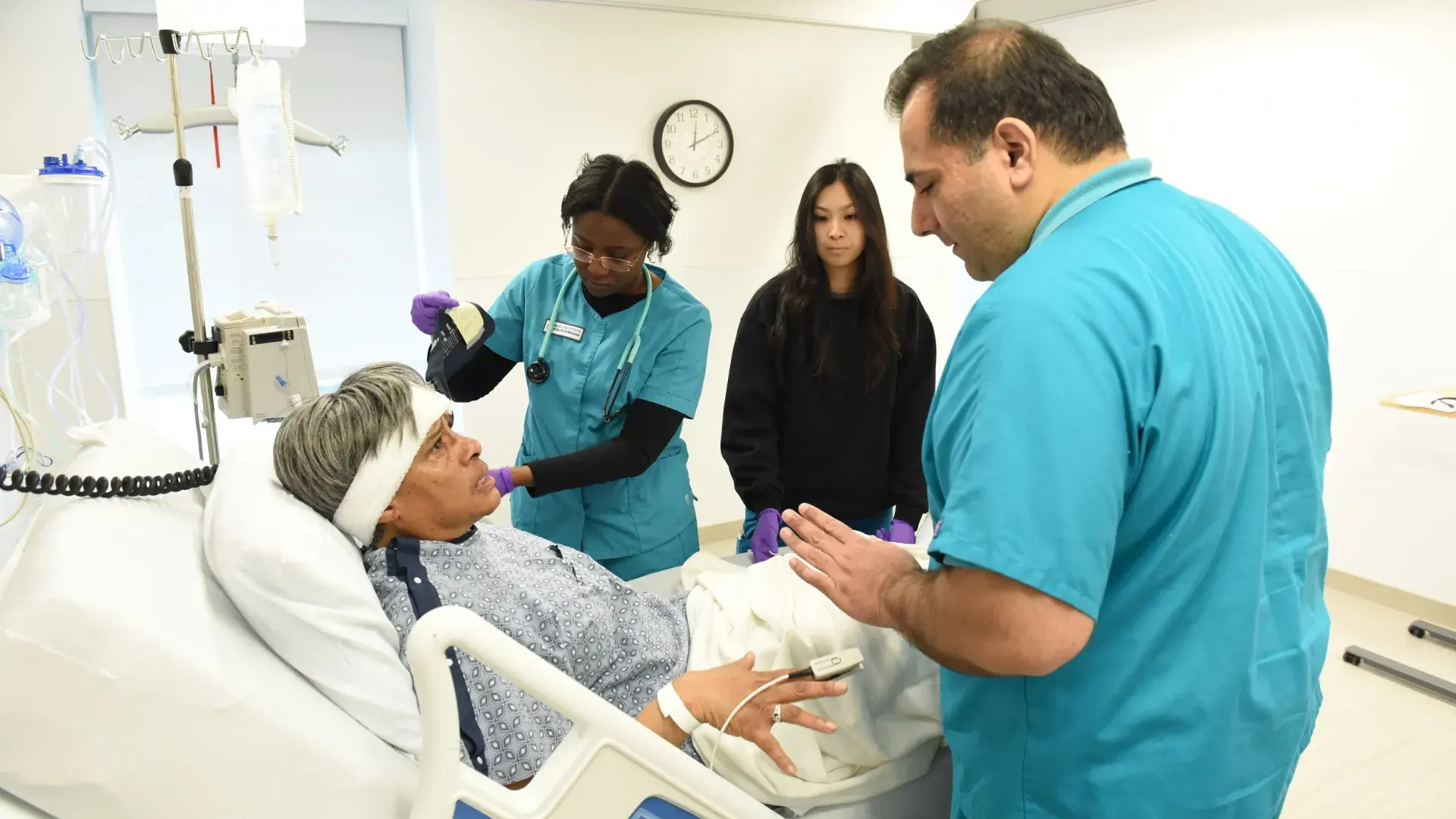 three people in scrubs stand around a woman in a hospital bed