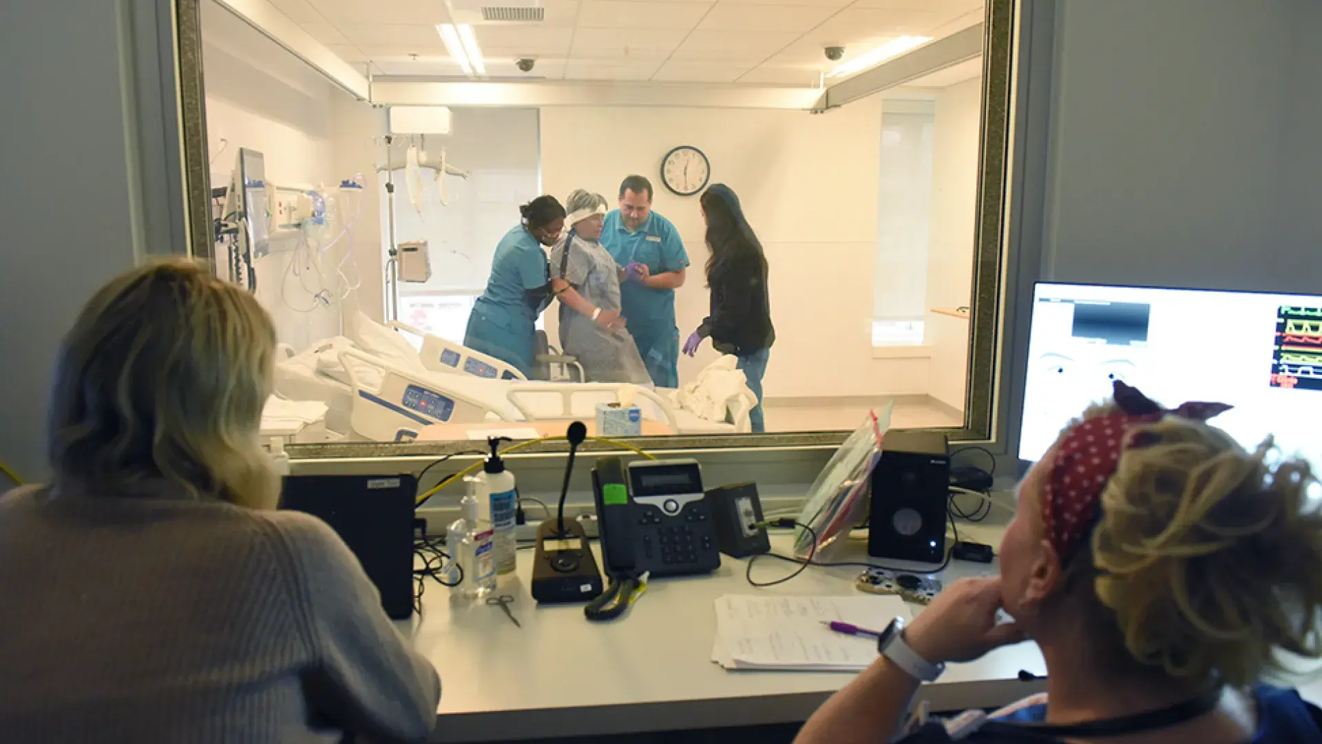 faculty observe nursing students with standardized patient through glass