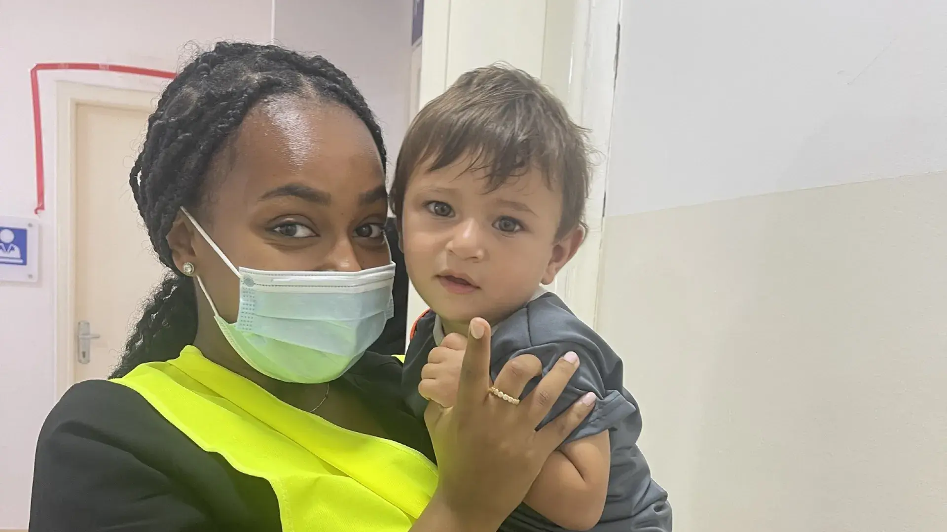 woman in yellow vest holds small boy